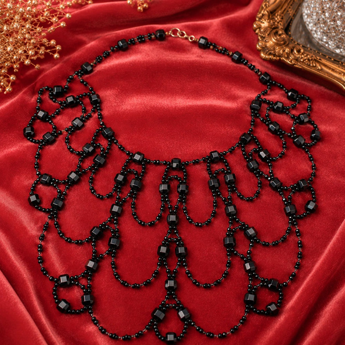 Black Royal handgefertigte Art-Déco Statement-Halskette aus schwarzen und klaren Glasperlen, dekorativ auf rotem Satin präsentiert. Die aufwendig gearbeitete Halskette besteht aus zahlreichen symmetrisch angeordneten Perlenschlaufen mit kleinen schwarzen Glasperlen und facettierten schwarzen Würfelperlen. Der breite, mehrreihige Aufbau verleiht dem Collier eine elegante und außergewöhnliche Optik für Abendmode und festliche Anlässe.