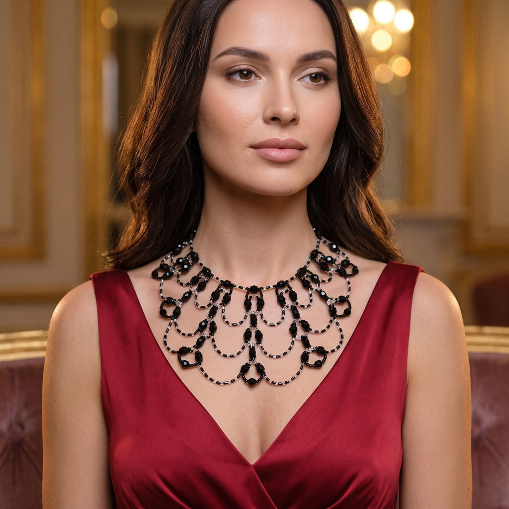 Black Royal handgefertigte Art-Déco Statement-Halskette aus schwarzen und klaren Glasperlen, getragen zu einem eleganten roten Abendkleid mit V-Ausschnitt. Das breite Collier mit symmetrisch angeordneten, geschwungenen Perlenschlaufen und facettierten schwarzen Glasperlen schmückt auffällig das Dekolleté. Eleganter Statement-Schmuck für Gala, Hochzeit, Abendveranstaltungen und besondere Anlässe.