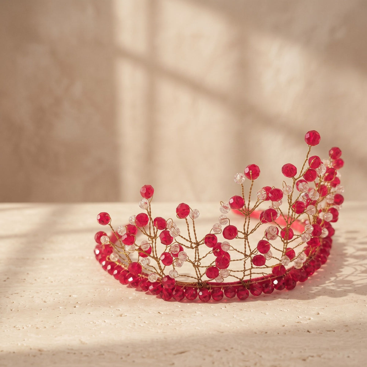 Handmade red and clear beaded crown with delicate gold wire branches, shown from the side in warm natural light to highlight the detailed beadwork.