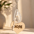 Handmade Hope bag charm featuring genuine clear quartz chips, natural wooden beads and white knotted cords, finished with a large wooden heart engraved with “HOPE” and a silver-tone lobster clasp. Photographed in warm natural sunlight against a soft neutral background, highlighting the transparent gemstones and natural wood texture.