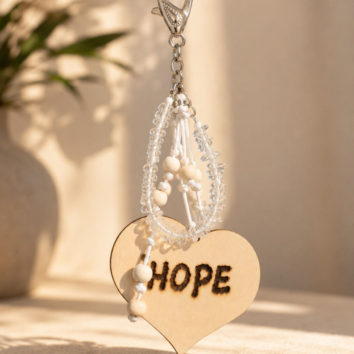 Handmade Hope bag charm featuring genuine clear quartz chips, natural wooden beads and white knotted cords, finished with a large wooden heart engraved with “HOPE” and a silver-tone lobster clasp. Photographed in warm natural sunlight against a soft neutral background, highlighting the transparent gemstones and natural wood texture.