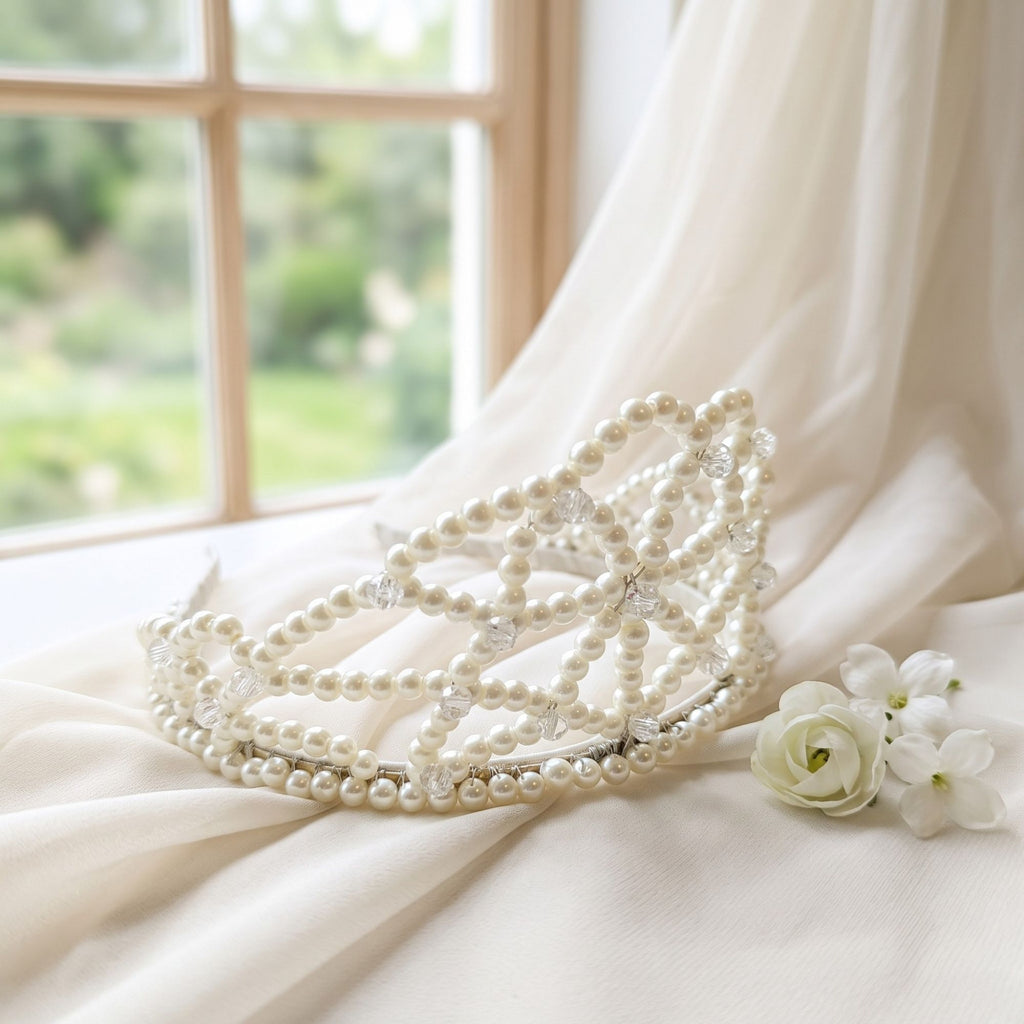 Ivory Dream handmade pearl bridal crown with ivory pearls and clear crystal beads, displayed on soft ivory fabric beside white flowers and a bright window.