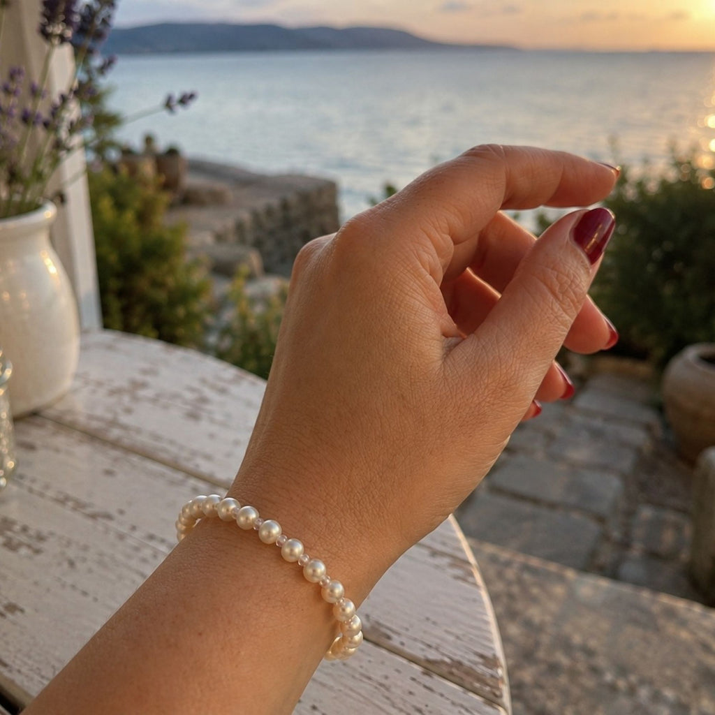 Lyra Moon white pearl bracelet with transparent crystal glass spacer beads, worn on the wrist in warm sunset light by the sea, an elegant minimalist handmade bracelet for everyday and special occasions.