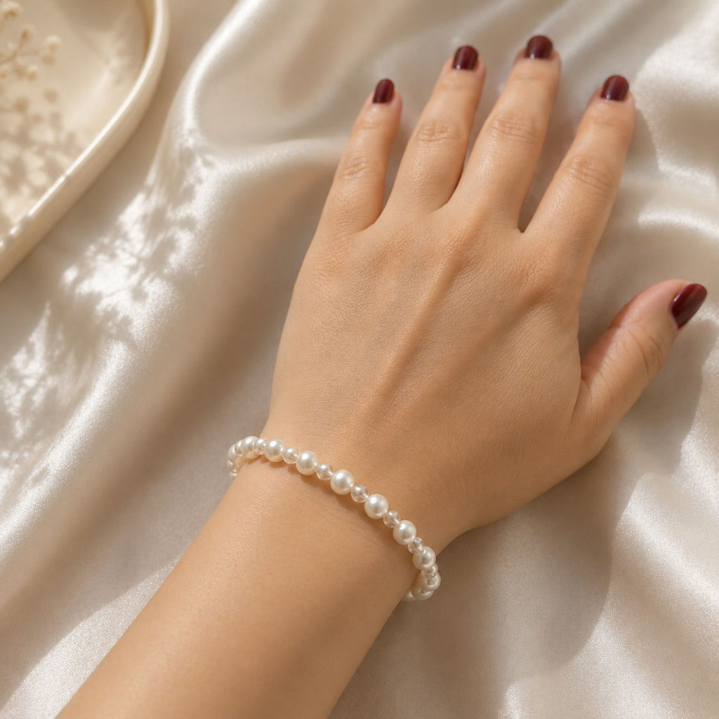 Lyra Moon white pearl bracelet worn on the wrist, featuring luminous white pearls with small transparent crystal glass spacer beads, a delicate minimalist handmade bracelet styled on soft ivory satin.
