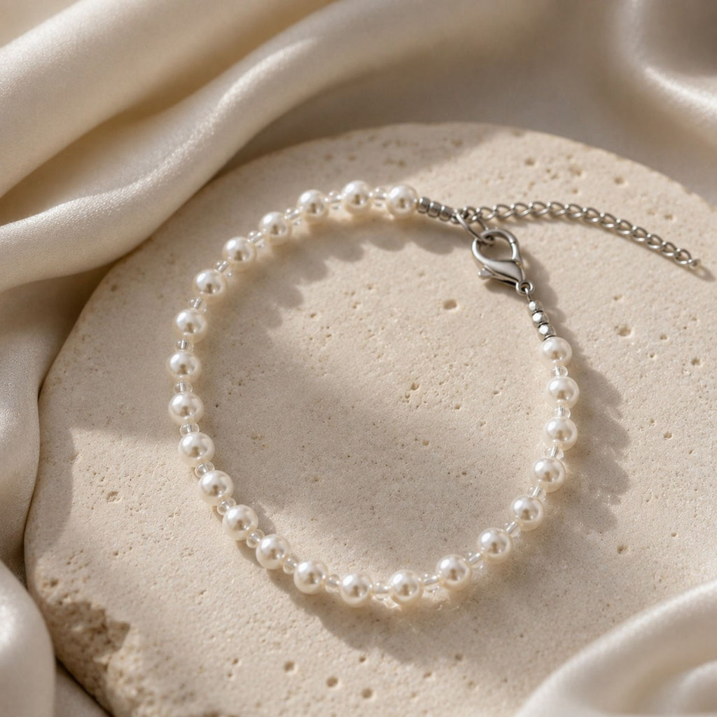 Lyra Moon elegant white pearl bracelet with delicate transparent crystal glass spacer beads, silver-tone lobster clasp and adjustable extension chain, displayed on a light stone surface with soft satin.