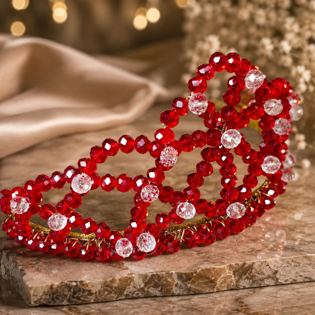 Handmade Red Queen beaded crown with faceted red glass beads, clear accent beads and gold-tone wire, elegantly displayed on a stone surface.