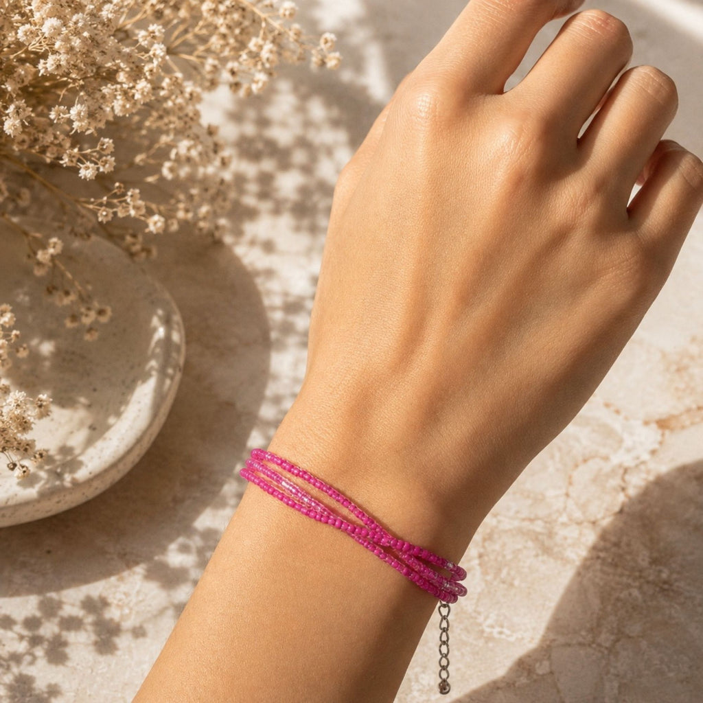 Rosalie three-strand pink glass bead bracelet worn on the wrist, featuring delicate clear bead accents and a silver-tone extender chain, photographed in warm natural sunlight beside soft dried flowers.