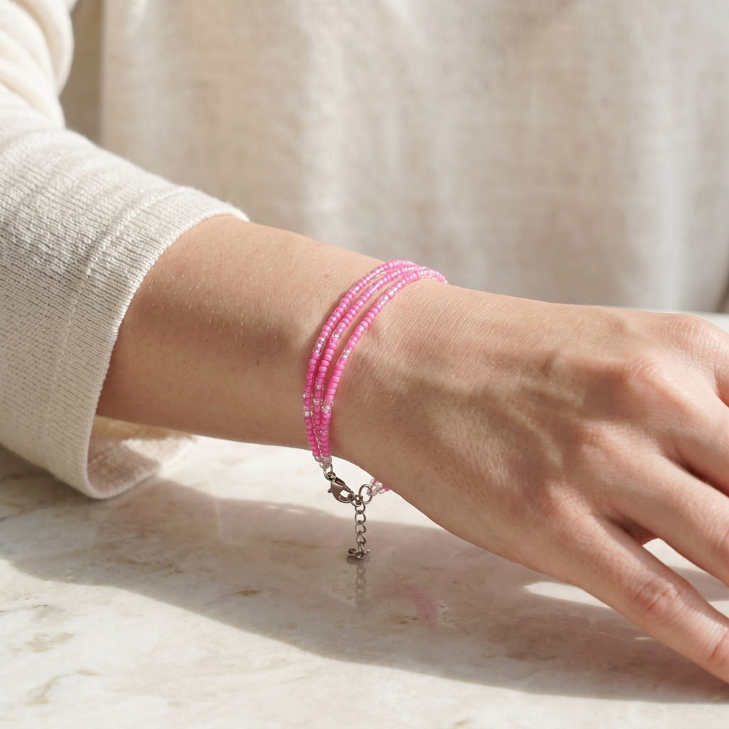 Rosalie three-strand pink glass bead bracelet worn on the wrist, featuring delicate clear bead accents, a silver-tone lobster clasp and adjustable extender chain, photographed in soft natural sunlight on a light marble surface.