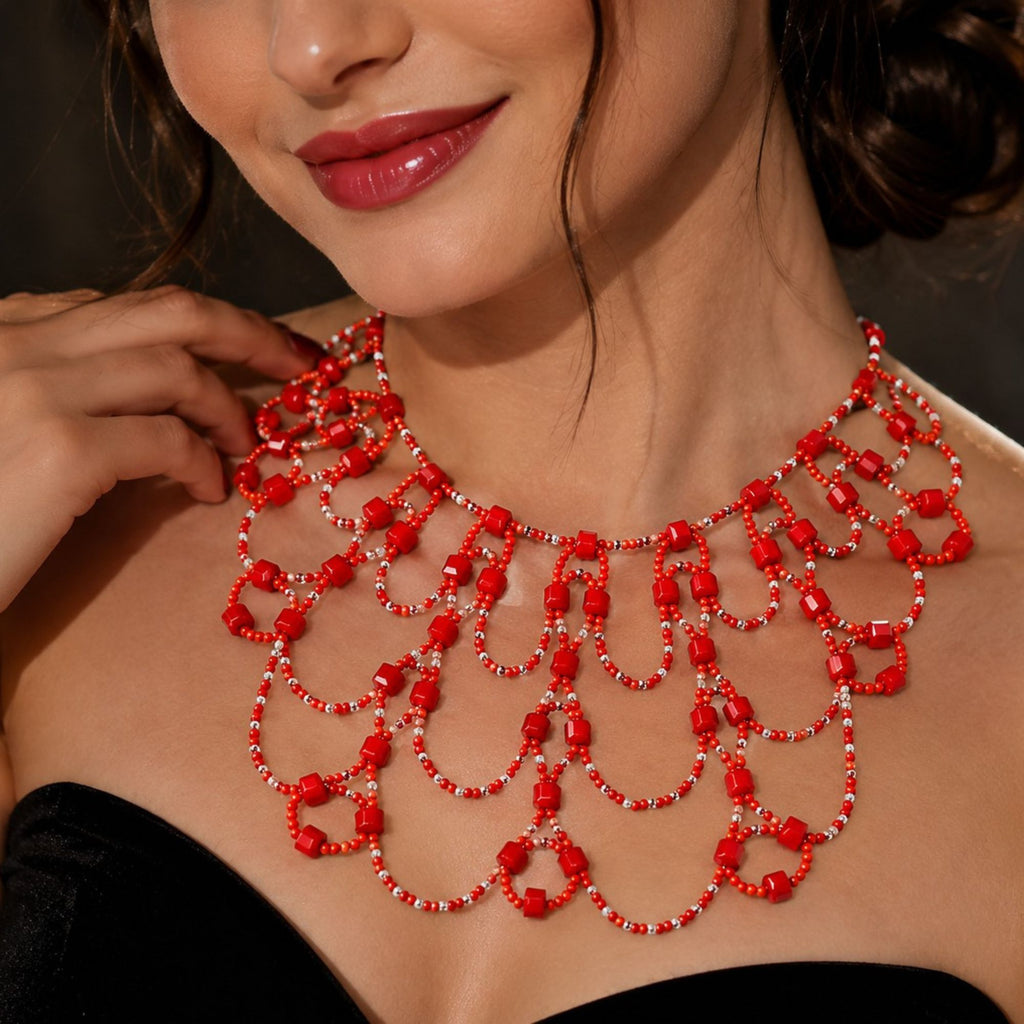 Scarlet Queen handgefertigte Statement-Halskette aus roten und transparenten Glasperlen, getragen zu einem schwarzen schulterfreien Kleid. Das aufwendige mehrreihige Art-Déco-Design mit geschwungenen Perlenbögen liegt dekorativ über dem Dekolleté und zeigt die Größe und Passform der roten Glasperlenkette.
