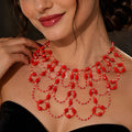 Scarlet Queen handgefertigte Statement-Halskette aus roten und transparenten Glasperlen, getragen zu einem schwarzen schulterfreien Kleid. Das aufwendige mehrreihige Art-Déco-Design mit geschwungenen Perlenbögen liegt dekorativ über dem Dekolleté und zeigt die Größe und Passform der roten Glasperlenkette.