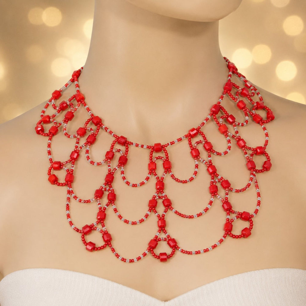 Scarlet Queen Statement-Halskette aus roten und transparenten Glasperlen auf einer hellen Schmuckbüste. Das handgefertigte mehrreihige Design besteht aus kunstvoll angeordneten Perlenbögen und roten Würfelperlen und zeigt die Form, Länge und auffällige Wirkung der Halskette besonders deutlich.