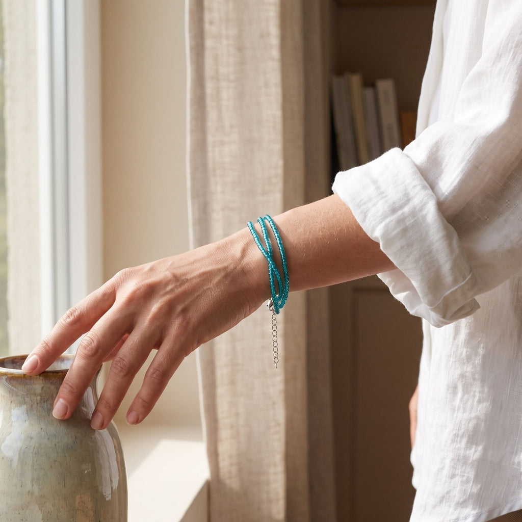 Selva handmade three-strand bracelet with delicate transparent turquoise glass seed beads, worn on the wrist in a softly lit indoor setting. The three fine turquoise strands create an elegant layered look, while the silver-tone adjustable extension chain hangs naturally below the wrist. A white linen shirt and warm neutral interior emphasize the bracelet’s fresh, minimalist and versatile everyday style.